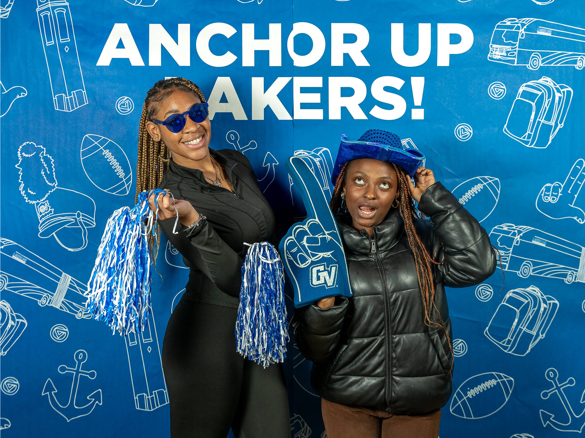 two individuals, one on the left holding two pompoms wearing blue sunglasses , one on the right holding a gvsu foam finger wearing a blue cowboy hat